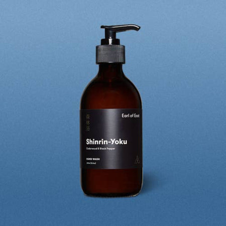 Amber glass bottle with pump and black label on a blue background. Earl of East shinrin-yoku hand wash.