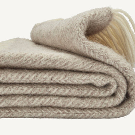 Folded neutral toned hazel throw in fishbone pattern on a white background