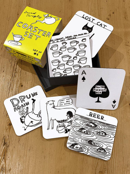 Set of coasters with humorous designs on a wooden surface, including a box labeled 'Coaster Set'.