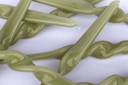 A jumble of leaf green twisted taper candles on a white background