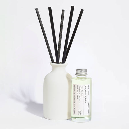 Elegant, white ceramic and reusable diffuser with black reeds and a glass bottle with aluminium screw top lid on a light background.