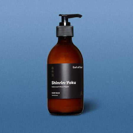 Amber glass bottle with pump dispenser on a blue background. Earl of East Shinrin-Yoku hand balm.