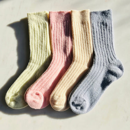 Four pairs of colourful cashmere socks, yellow, pink, cream and blue arranged in a row on a light surface.
