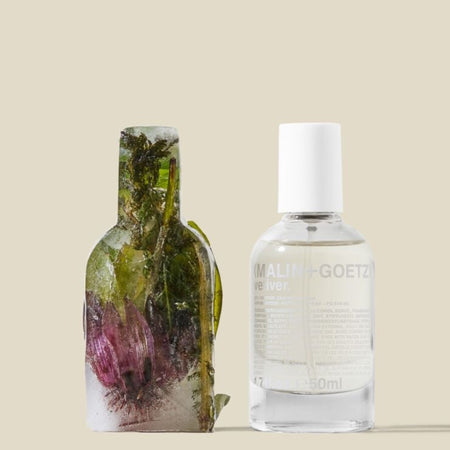 Two bottles, one with a natural plant design and the other vetiver eau de parfum with text, on a beige background.