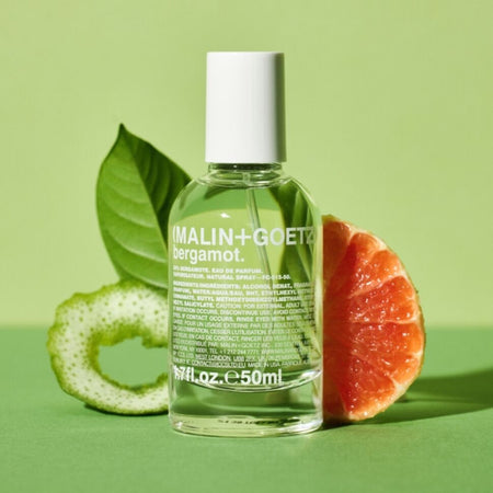 MALIN+GOETZ bergamot eau de parfum bottle with a sliced grapefruit and leaf on a green background