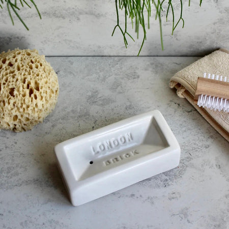 White London Brick soap dish with indented 'London' branding on a gray surface with cleaning tools. Perfect for design lovers who appreciate function with an industrial edge.