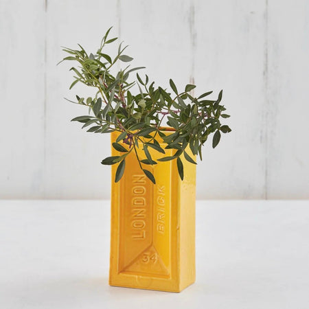 Yellow London brick-shaped vase with green plant against a white background