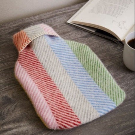Colorful striped hot water bottle and cover cover on a wooden surface with an open book and cup of coffee.
