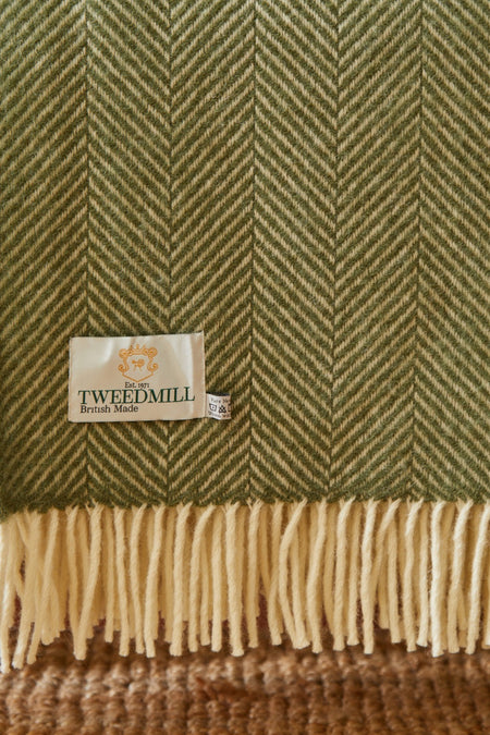 Close-up of a green Tweedmill woollen throw with a fishbone pattern and brand label.