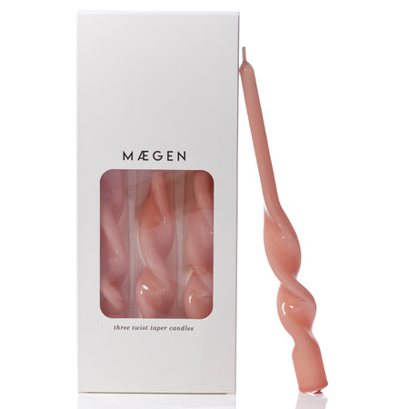 Plaster pink twisted taper candle leaning against branded Máegen white box packaging with see through window on a white background