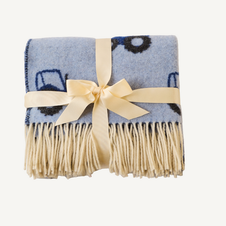 Blue baby blanket with tractor design with cream fringe and a cream ribbon tied in a bow on a white background
