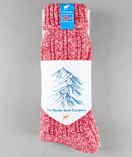 Red knitted Icelandic Saga socks with an Iceland flag brand label and white packaging with mountain design on a gray background. Lambswool and cotton rich to get you through the cold Arctic nights.