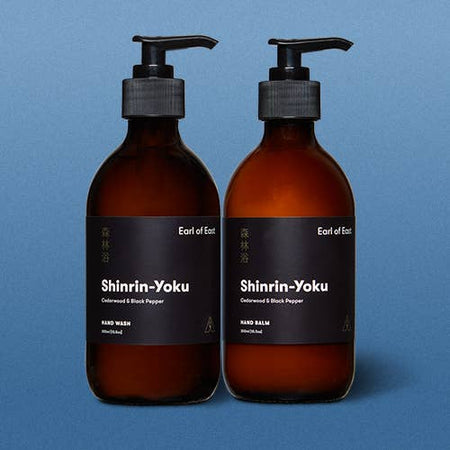 Two amber glass bottles with pump and black label on a blue background. Earl of East shinrin-yoku hand wash and hand balm.