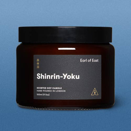 Scented soy candle jar labeled 'Shinrin-Yoku' by Earl of East on a blue background. A large glass amber jar with a screw top lid.