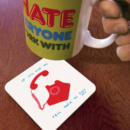 Mug with colorful text and a hand holding it, coaster with red design on wooden surface