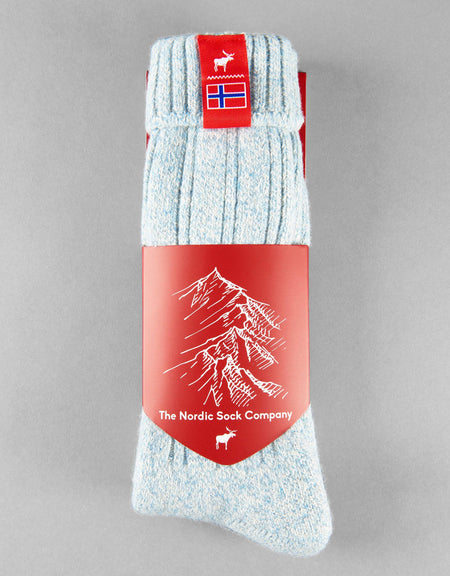 Pale blue sock with red packaging featuring a mountain design and Norwegian flag, on a gray background.