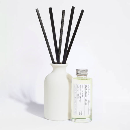 Elegant, white ceramic and reusable diffuser with black reeds and a glass bottle with aluminium screw top lid on a light background