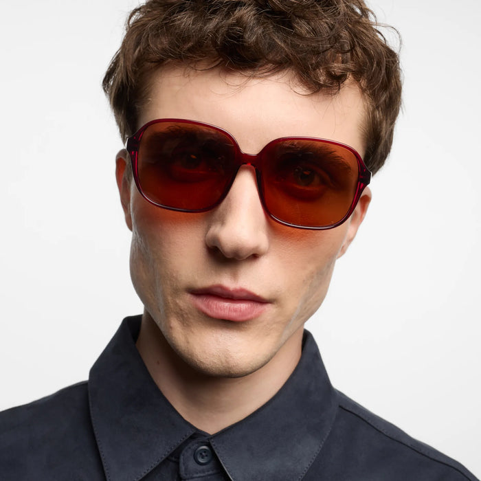 Person wearing red sunglasses with a neutral background