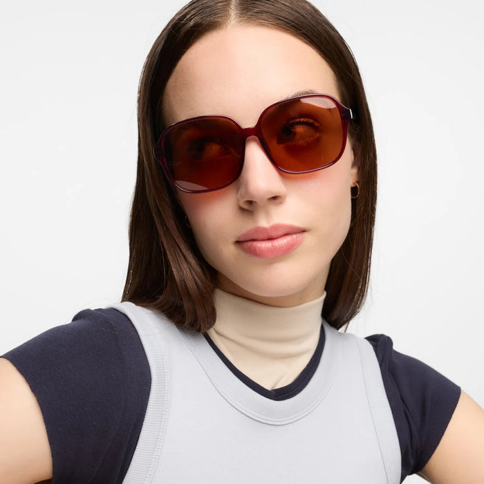 Woman wearing oversized red framed sunglasses with a plain background