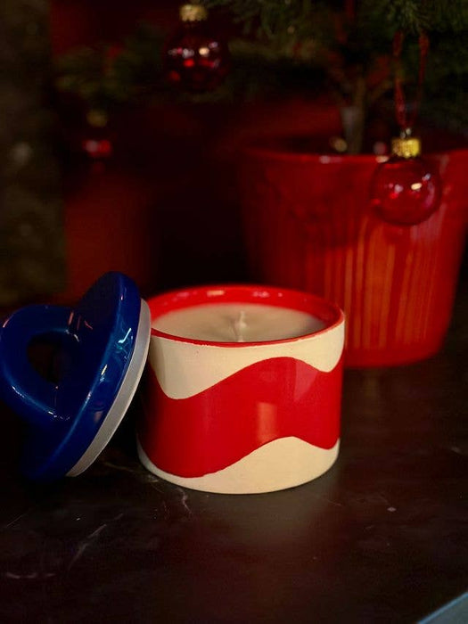 Red and white ceramic candle with blue lid on a dark surface, Christmas decorations in the background