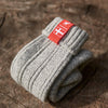 Folded Sky grey knitted Danish Hygge socks with a Danish flag brand label on a wooden log background. Lambswool and cotton rich to get you through the cold Arctic nights.
