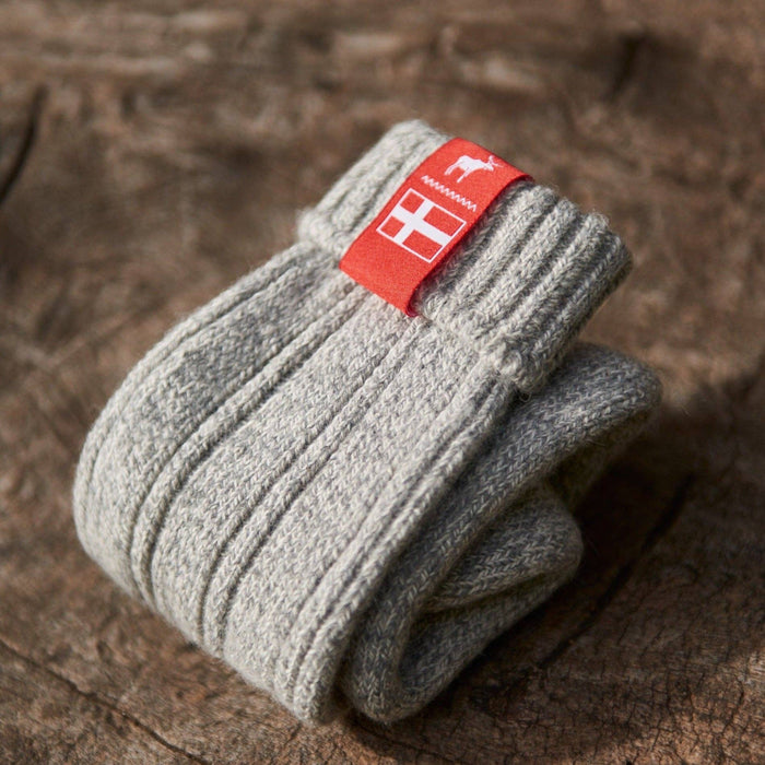 Folded Sky grey knitted Danish Hygge socks with a Danish flag brand label on a wooden log background. Lambswool and cotton rich to get you through the cold Arctic nights.