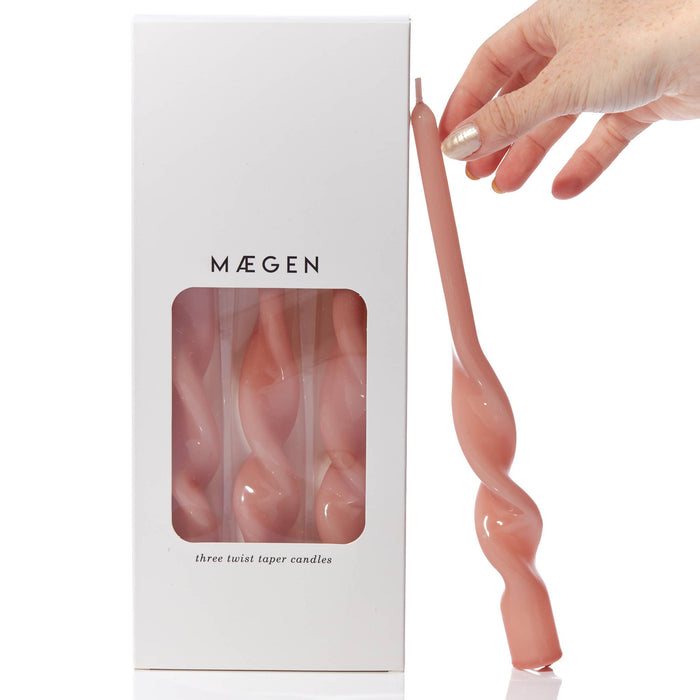 Máegen candle packaging with a hand holding a pink twisted candle.