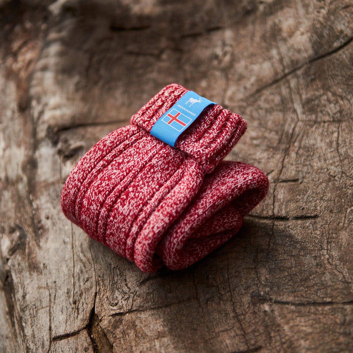 Folded red knitted Icelandic Saga socks with an Iceland flag brand label on a wooden log background. Lambswool and cotton rich to get you through the cold Arctic nights.