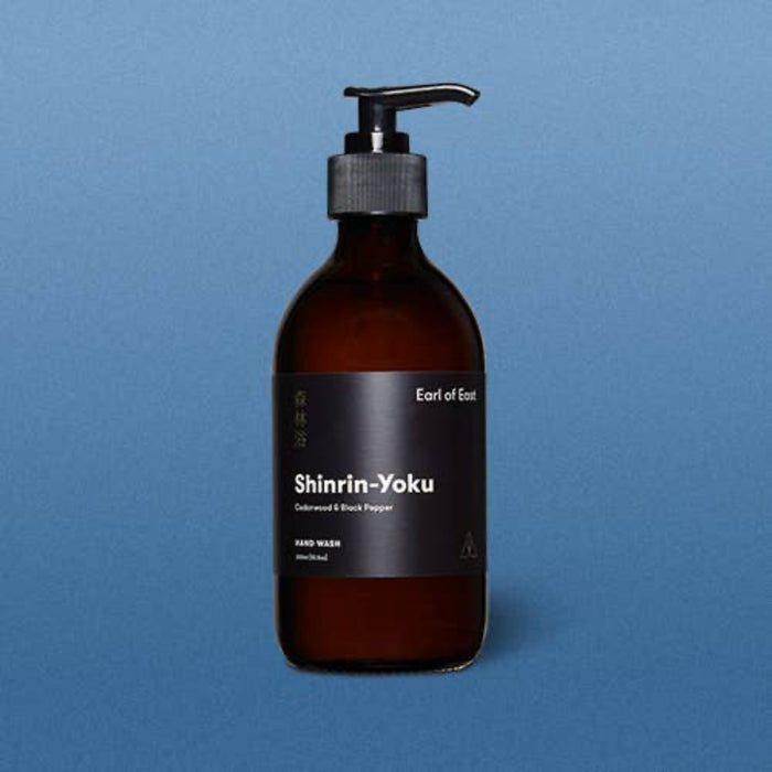 Amber glass bottle with pump and black label on a blue background. Earl of East shinrin-yoku hand wash.
