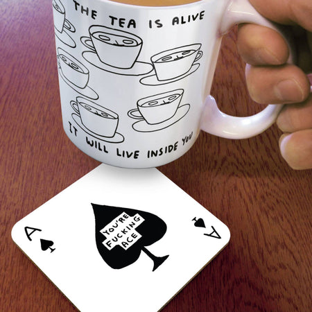 White mug with black tea illustrations and text, held over a coaster with a black and white design.