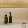 Two amber glass bottles with pump and black label located on a kitchen countertop. Earl of East shinrin-yoku hand wash and hand balm.
