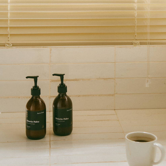 Two amber glass bottles with pump and black label located on a kitchen countertop. Earl of East shinrin-yoku hand wash and hand balm.