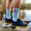 Man hiking by a Norwegian lake wearing premium pale blue socks with a red flag design.