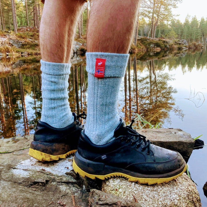 Man hiking by a Norwegian lake wearing premium pale blue socks with a red flag design.