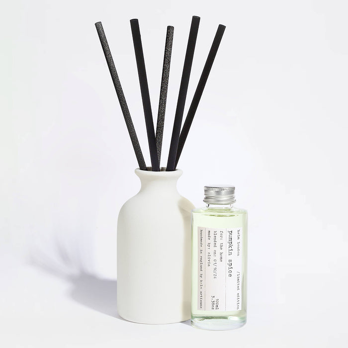 Elegant, white ceramic and reusable diffuser with black reeds and a glass bottle with aluminium screw top lid on a light background.
