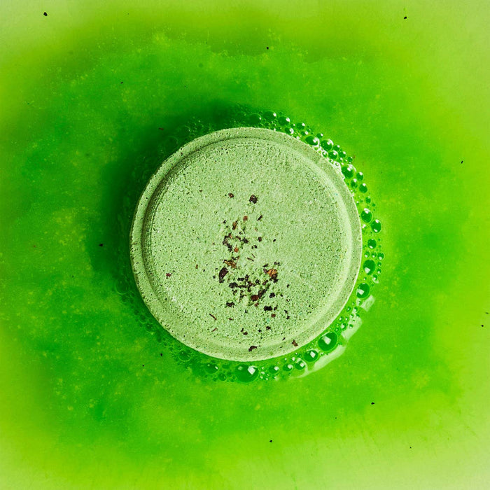 A green peppermint and herb shower steamer bubbling on a green background