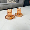 Two amber-colored glass candle holders on a white surface with a gray sofa in the background.