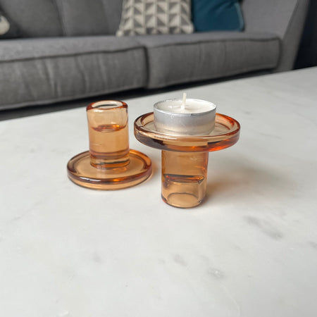 Two amber glass candle holders with candles on a light surface.