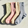 Four pairs of colourful cashmere socks, yellow, pink, cream and blue arranged in a row on a light surface.
