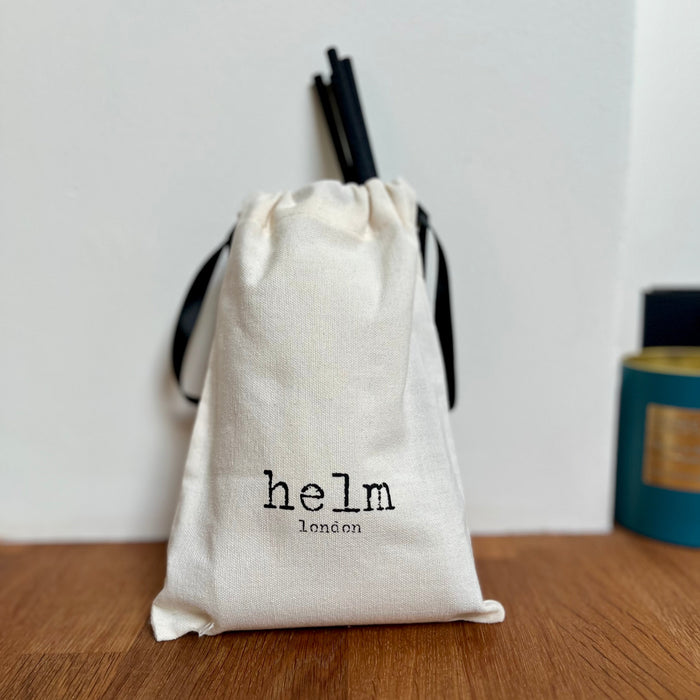 Helm diffuser in a drawstring cotton bag with 'helm london' branding on a wooden surface.