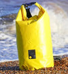 Yellow dry bag with a logo on a beach with waves in the background