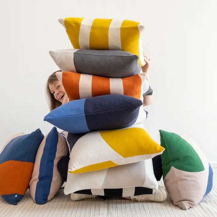Person peeking out from a stack of colorful pillows on a white background