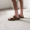 Brown sandals worn with pink cashmere socks on a light gray carpet