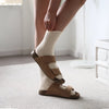 Person wearing cream cashmere socks and brown sandals indoors.