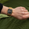 Gold watch on a wrist with a green background