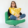 Person sitting on a green chair holding a yellow cushion with leaf pattern against a white background