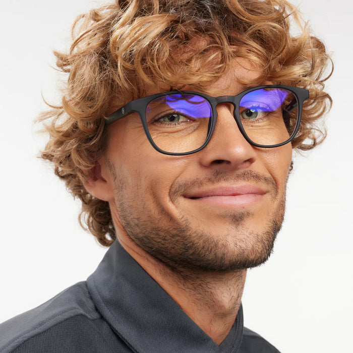 Man wearing black-framed glasses with blue light reflection on a light gray background