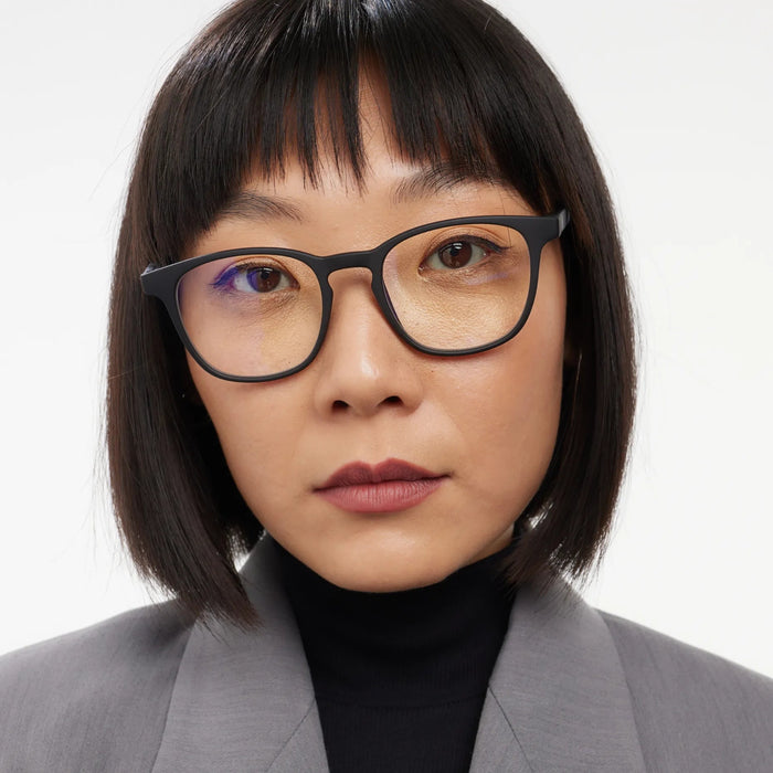Person wearing glasses and a gray blazer against a white background
