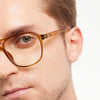 Close-up of a person wearing olive eyeglasses with a neutral background