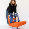 Woman holding a colourful floral cushion next to an orange chair on a white background